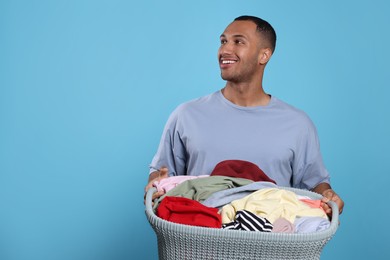 Photo of Happy man with basket full of laundry on light blue background. Space for text