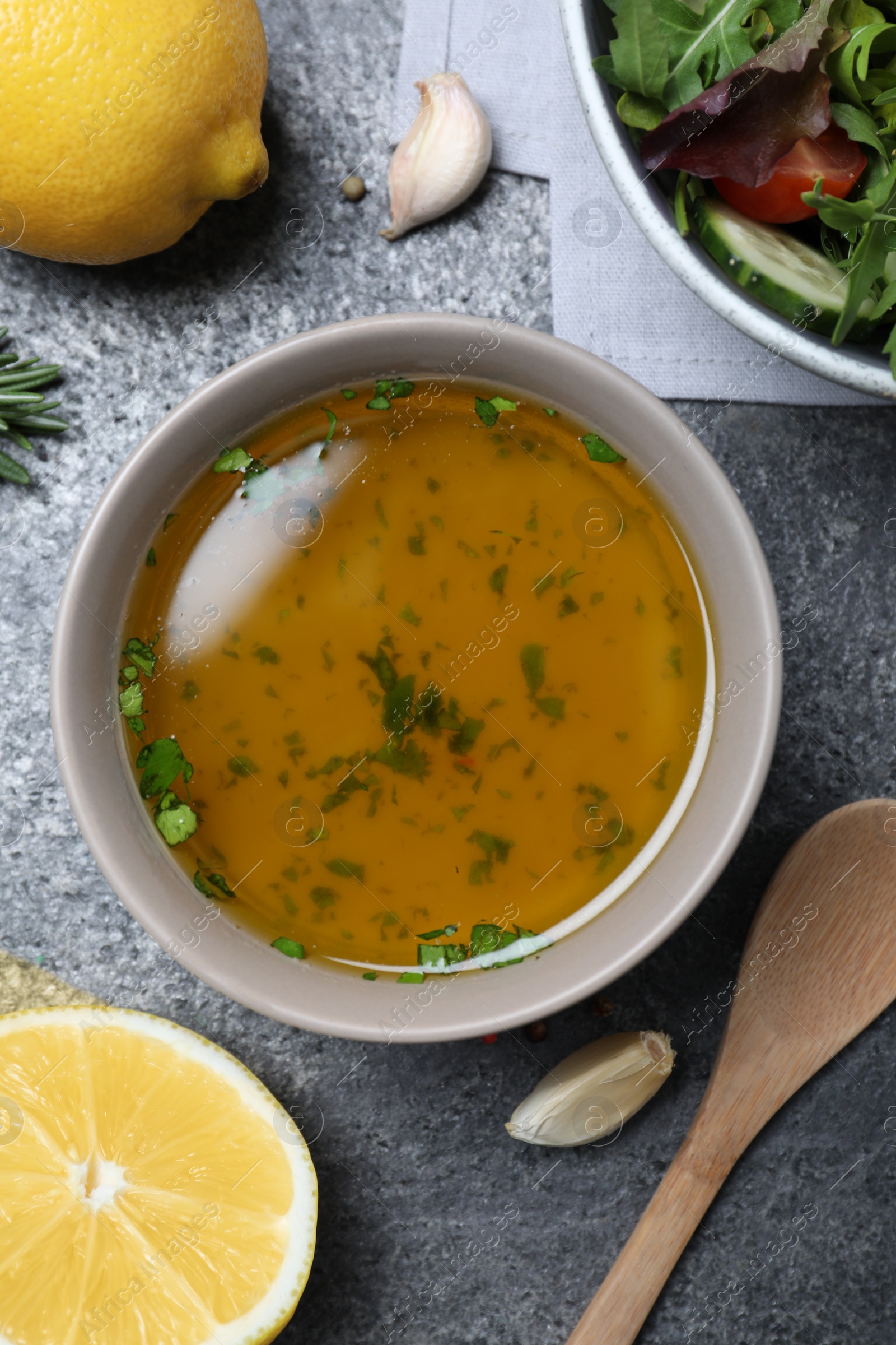 Photo of Bowl with lemon dressing near salad on grey table, flat lay. Delicious salad dressing