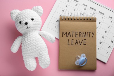 Photo of Toy bear, calendar, notepad with text Maternity Leave and pacifier on pink background, flat lay
