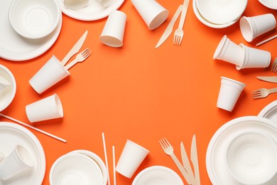 Photo of Frame of disposable tableware on orange background, flat lay. Space for text
