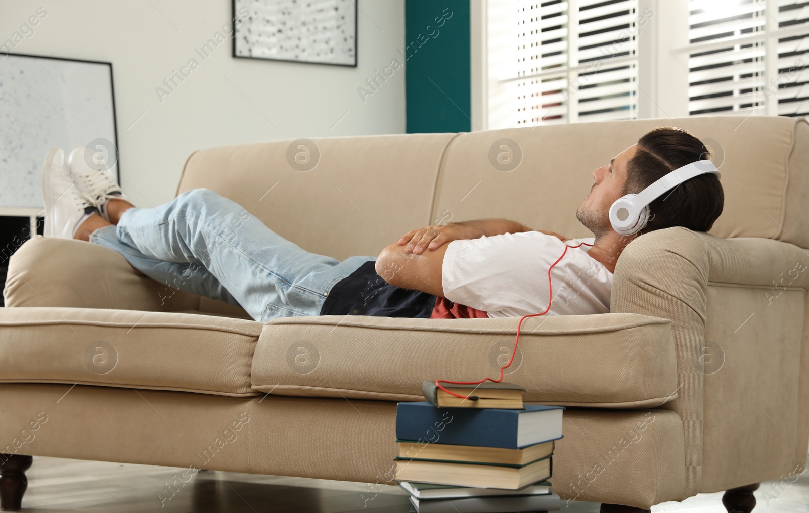 Photo of Man with headphones connected to book
on sofa at home. Audiobook concept