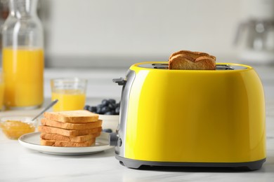 Photo of Yellow toaster with roasted bread slices, jam, juice and blueberries on white marble table