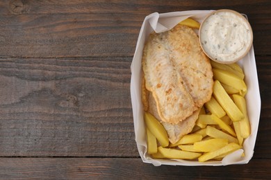 Photo of Delicious fish and chips with tasty sauce in paper box on wooden table, top view. Space for text