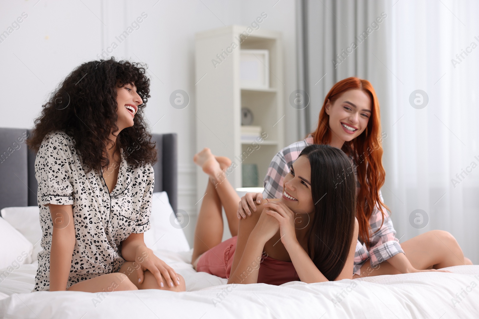 Photo of Happy young friends spending time together on bed at home