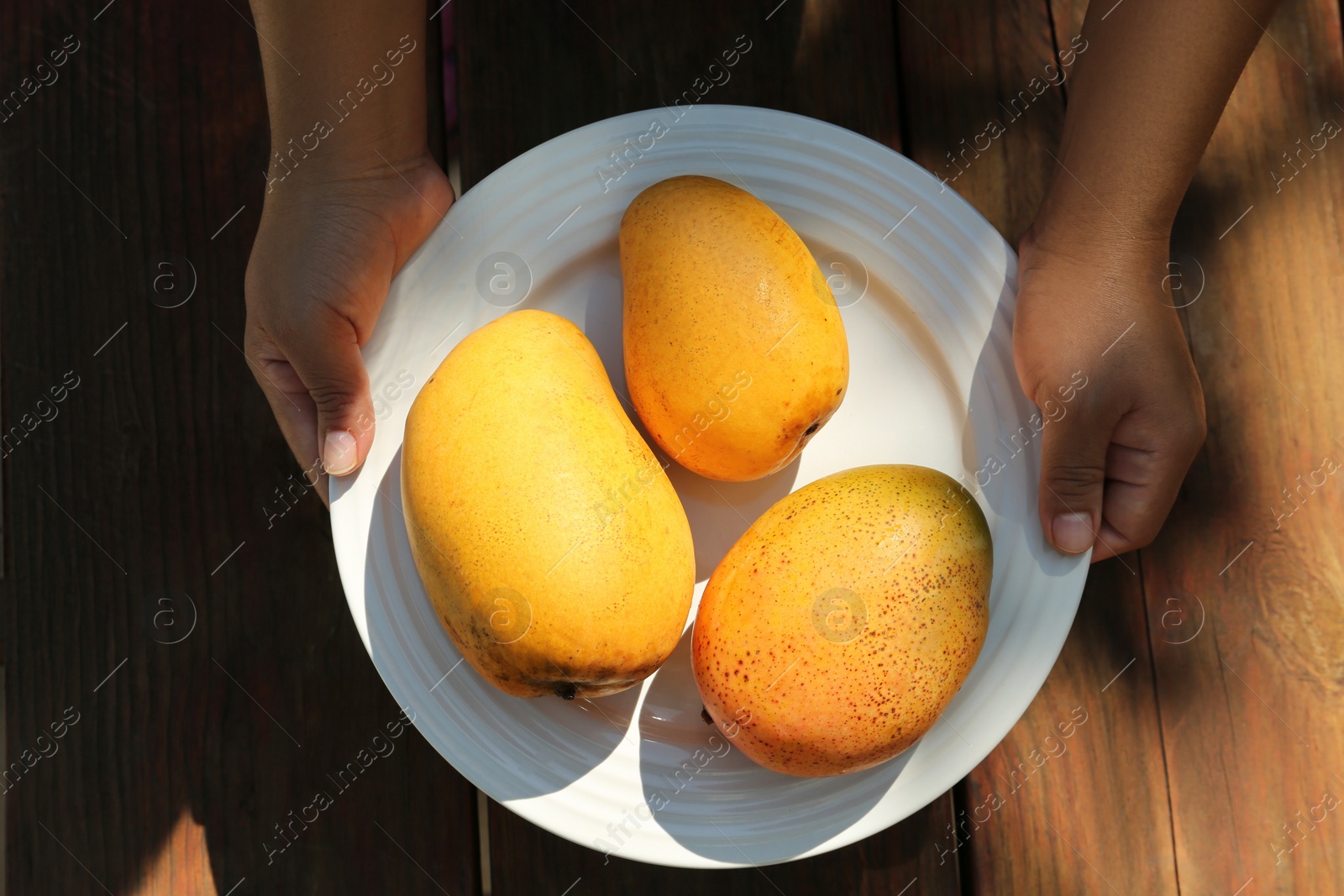 Photo of Woman holding plate with tasty mangoes at wooden table, top view