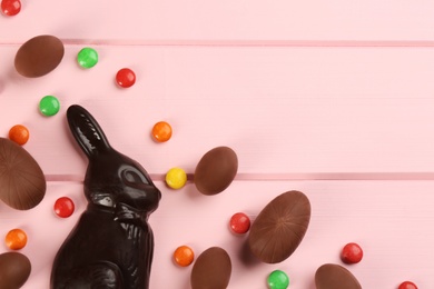 Photo of Dark chocolate Easter bunny, candies and eggs on pink wooden table, flat lay. Space for text