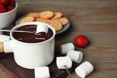 Photo of Fondue pot with chocolate and marshmallow on wooden table