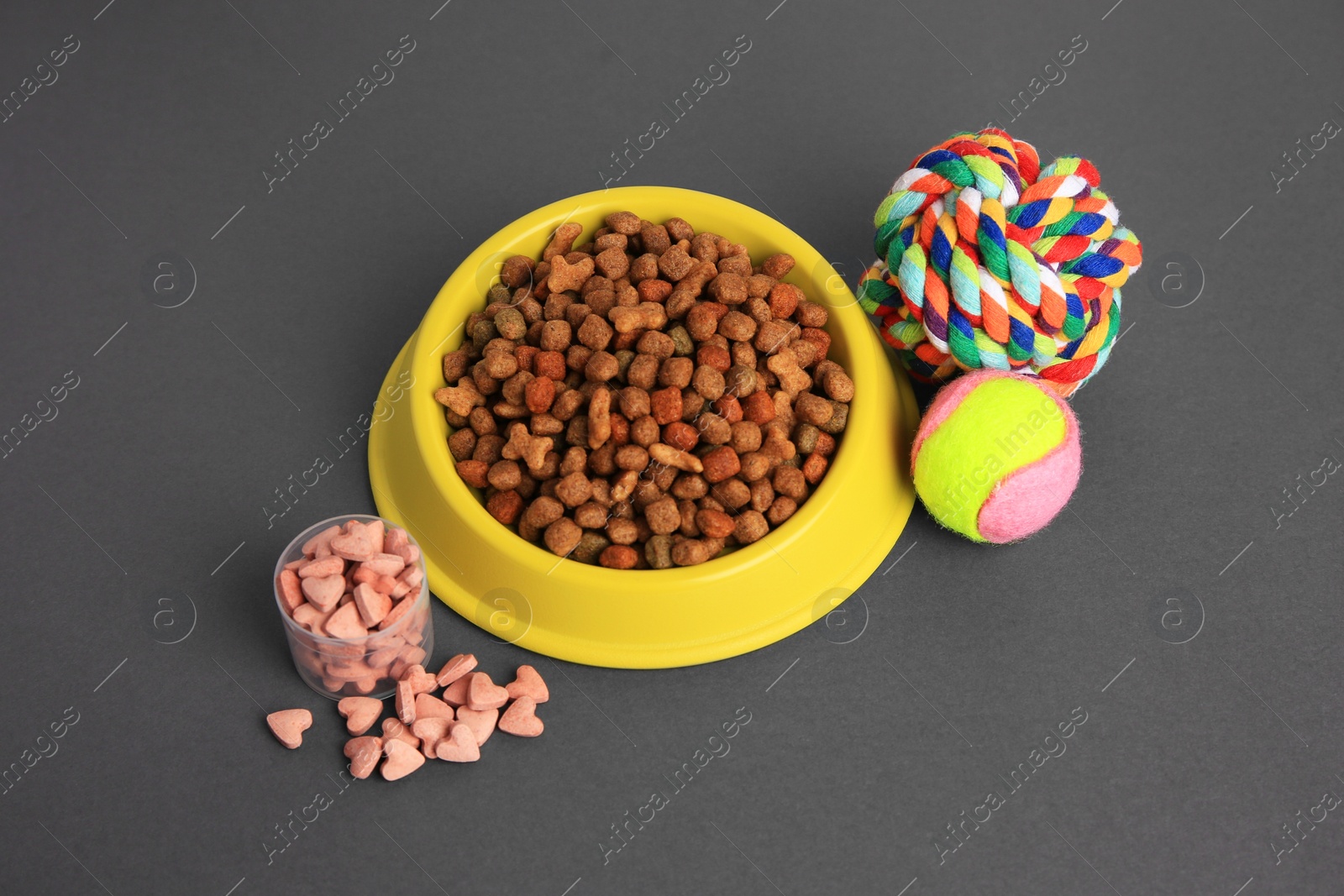 Photo of Vitamins, toys and dry pet food in bowl on grey background, above view