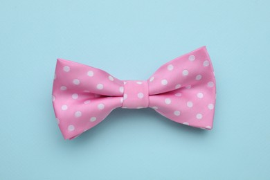 Stylish pink bow tie with polka dot pattern on light blue background, top view