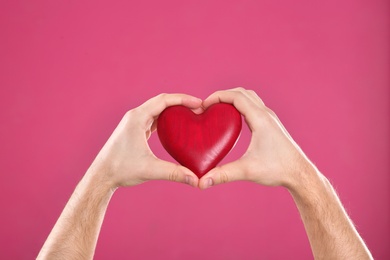 Photo of Man holding decorative heart in hands on color background, closeup