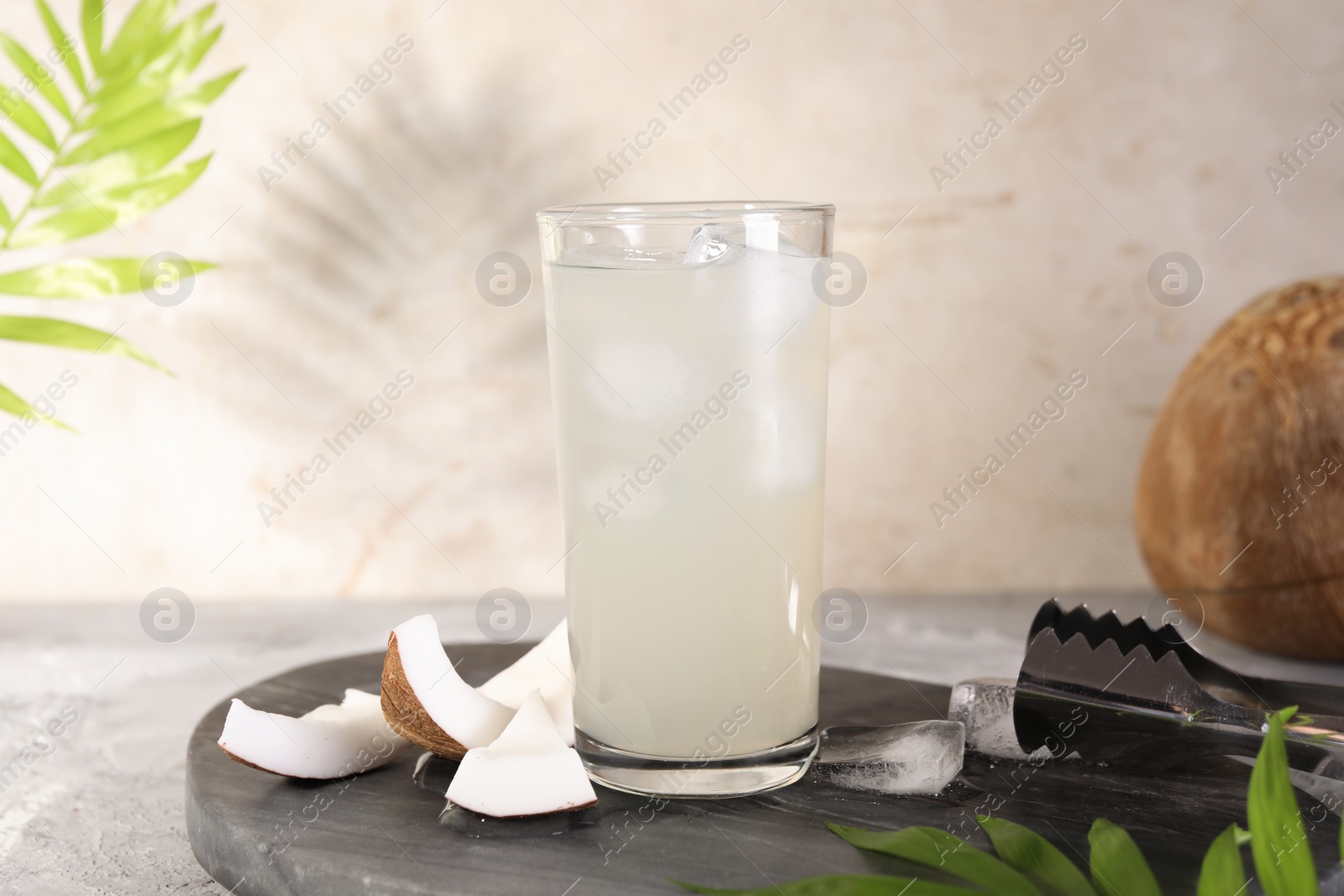 Photo of Glass of coconut water, ice cubes and nuts on grey table