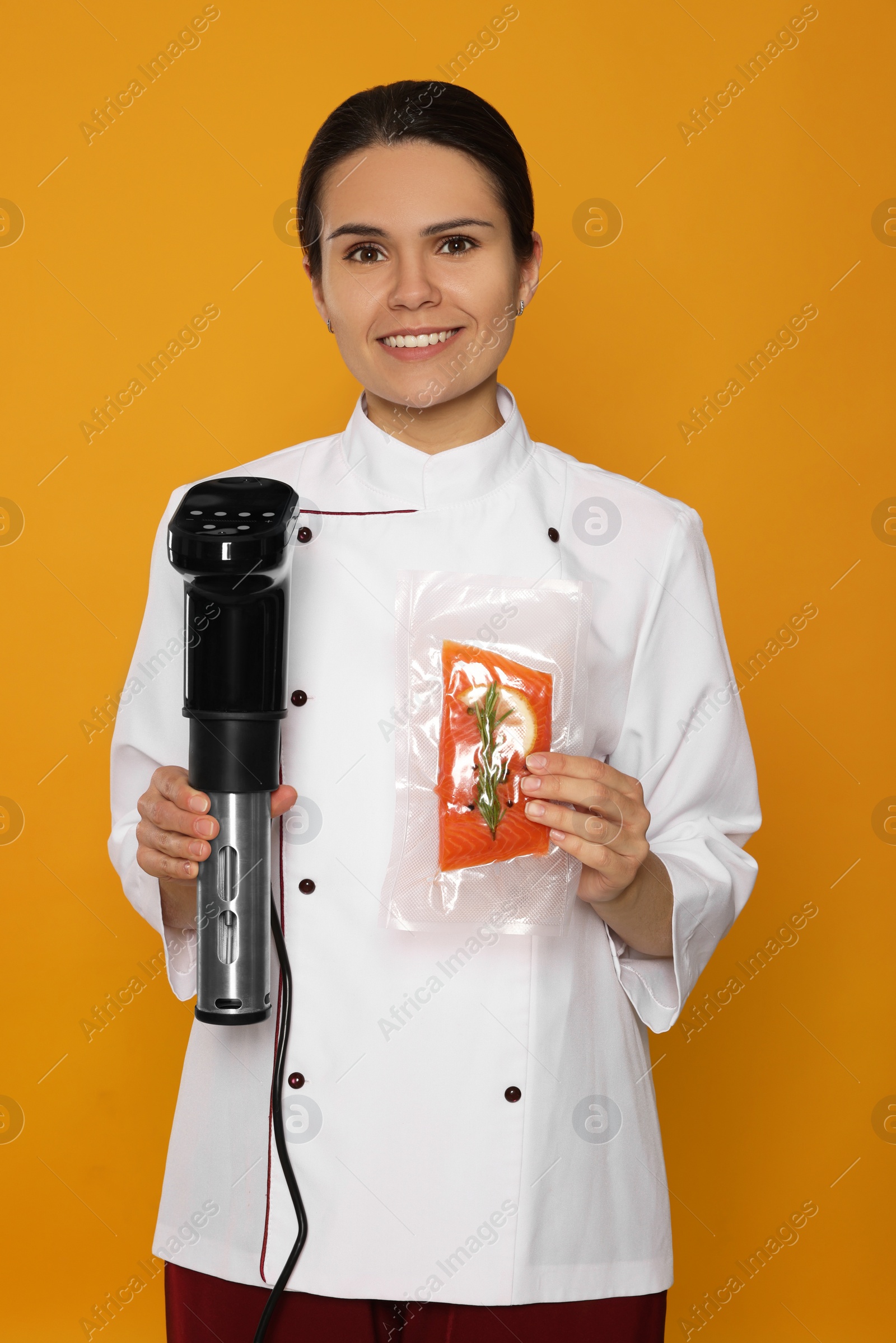 Photo of Chef holding sous vide cooker and salmon in vacuum pack on orange background