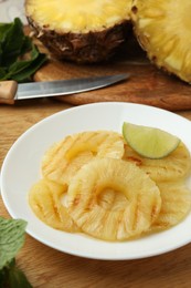 Photo of Tasty grilled pineapple slices and piece of lime on wooden table, closeup