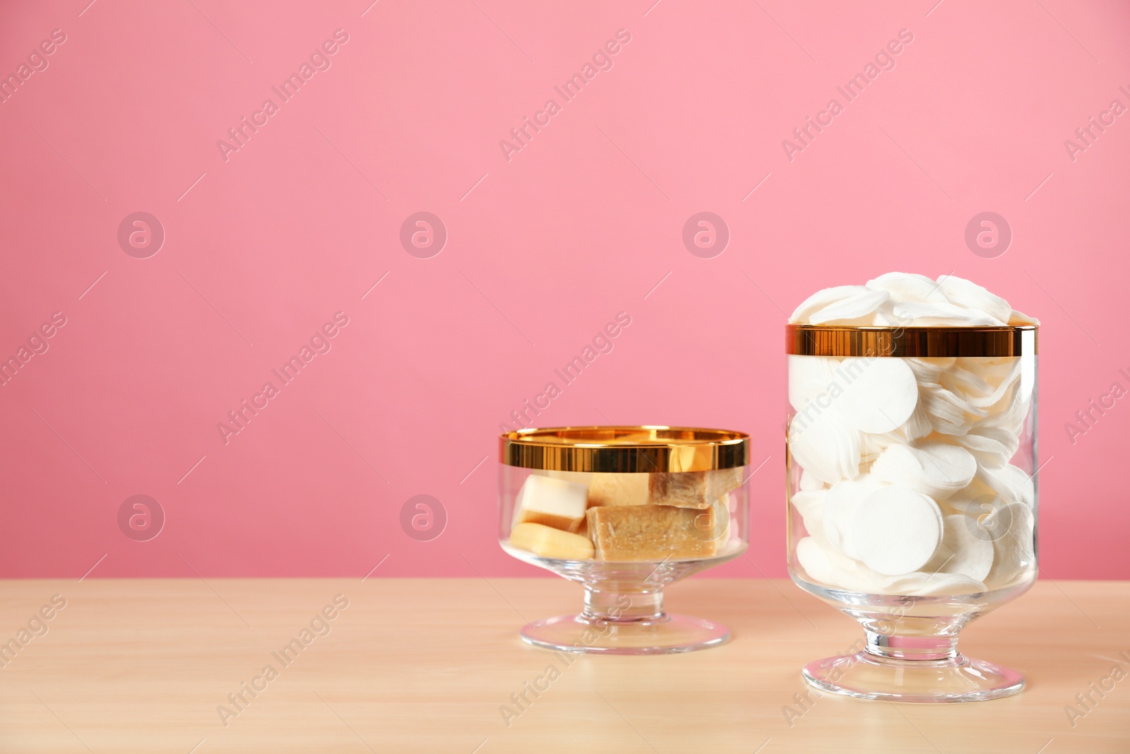 Photo of Jars with cotton pads and soap on wooden table against pink background. Space for text