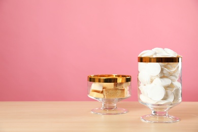 Jars with cotton pads and soap on wooden table against pink background. Space for text