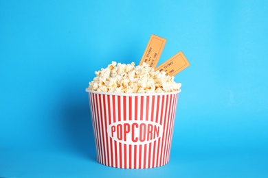 Photo of Bucket of fresh tasty popcorn and tickets on color background. Cinema snack