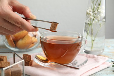 Woman adding brown sugar cube to aromatic tea at wooden table, closeup