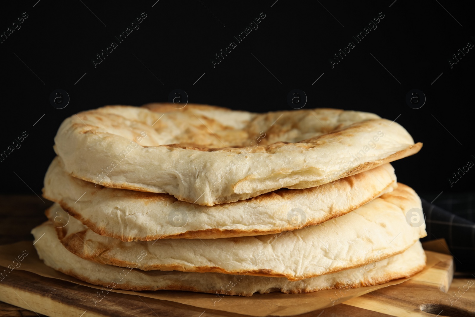 Photo of Delicious homemade pita bread on wooden table against black background, closeup