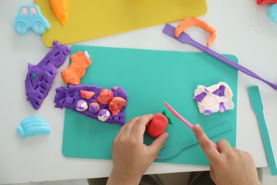 Photo of Little girl sculpting with play dough at white table, top view