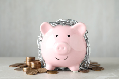 Photo of Piggy bank with steel chain and coins on grey marble table. Money safety concept