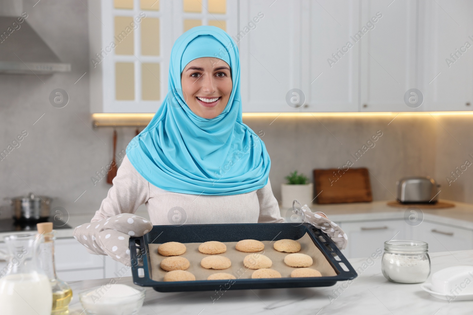 Photo of Portrait of Muslim woman near tray with cookies at white table in kitchen