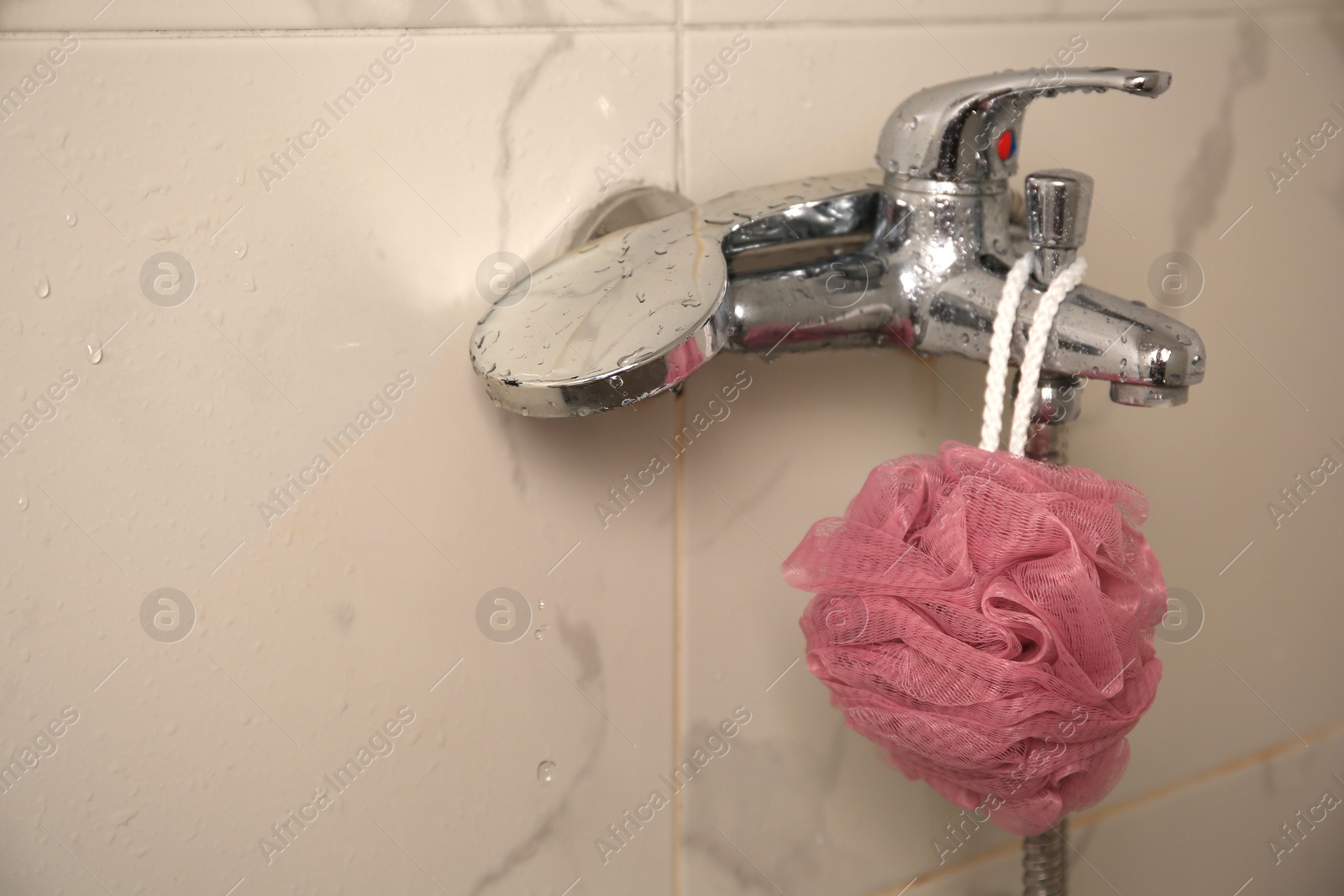 Photo of Pink shower puff hanging on faucet in bathroom. Space for text