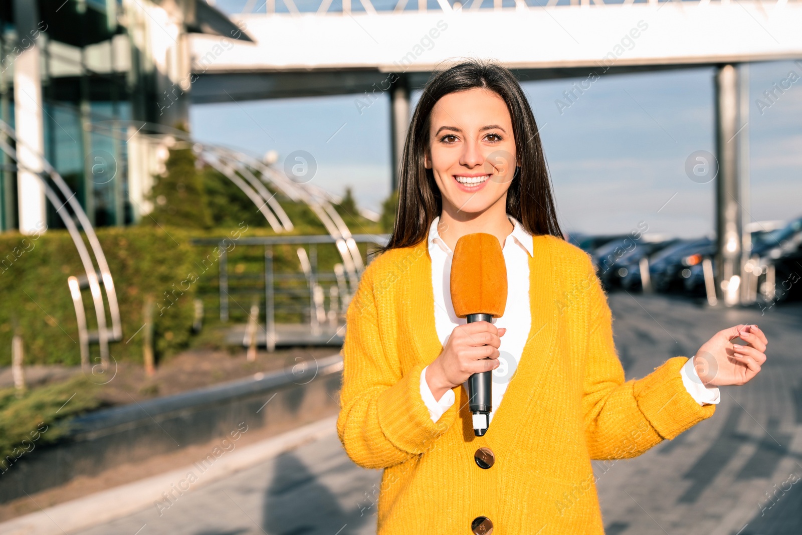 Image of Young female journalist with microphone working on city street