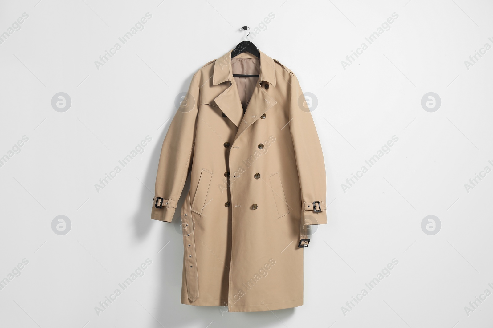 Photo of Hanger with beige trench coat on white wall