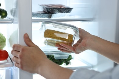 Photo of Young woman taking container with corn out of refrigerator, closeup