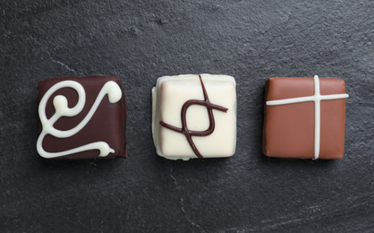 Photo of Different delicious chocolate candies on black table, flat lay