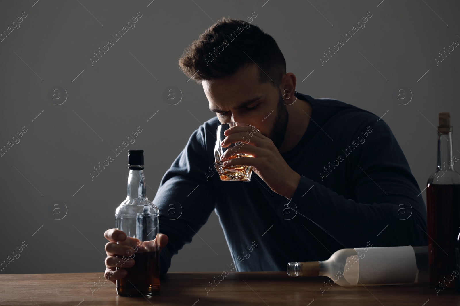 Photo of Addicted man drinking alcohol at wooden table indoors