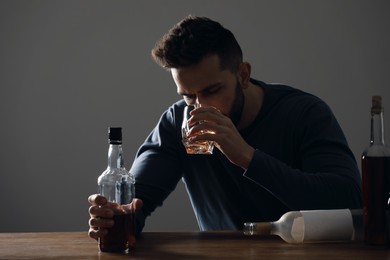 Photo of Addicted man drinking alcohol at wooden table indoors