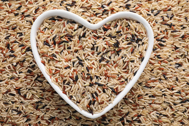 Photo of Mix of different brown rice and heart shaped bowl, top view