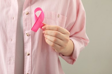 Photo of Woman with pink ribbon on light grey background, closeup. Breast cancer awareness