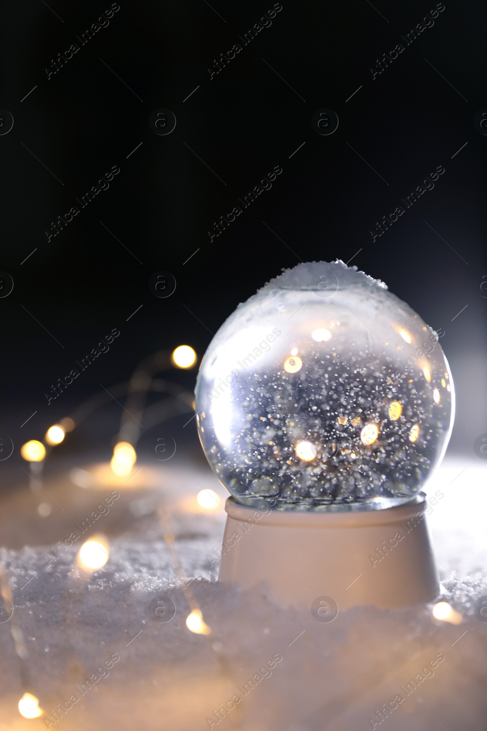 Photo of Crystal globe and Christmas lights on white snow outdoors