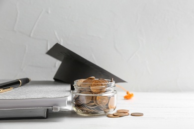 Jar of coins, notebooks and graduation hat on table against light background. Space for text