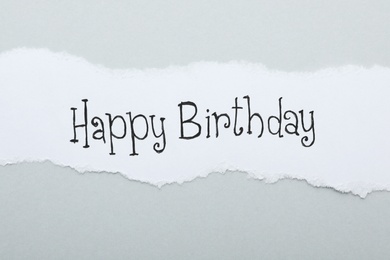 Photo of Sheet of paper with words HAPPY BIRTHDAY on light grey background, top view