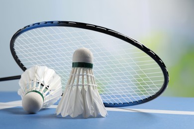 Feather badminton shuttlecocks and racket on blue table against blurred background, closeup