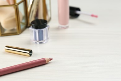 Photo of Lip pencils and other makeup products on white wooden table, space for text
