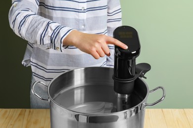 Sous vide cooking. Woman using thermal immersion circulator at wooden table, closeup