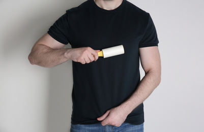 Man cleaning black t-shirt with lint roller on white background, closeup