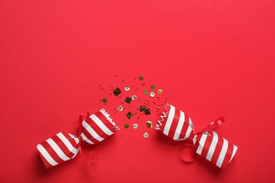 Photo of Open Christmas cracker with shiny confetti on red background, top view. Space for text