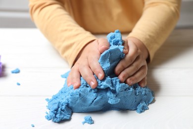 Photo of Little child playing with light blue kinetic sand at white wooden table, closeup