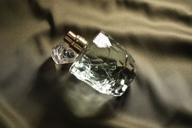 Photo of Luxury perfume in bottle on dark silk fabric, top view