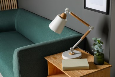 Photo of Stylish modern desk lamp, book and plant on wooden cabinet in living room