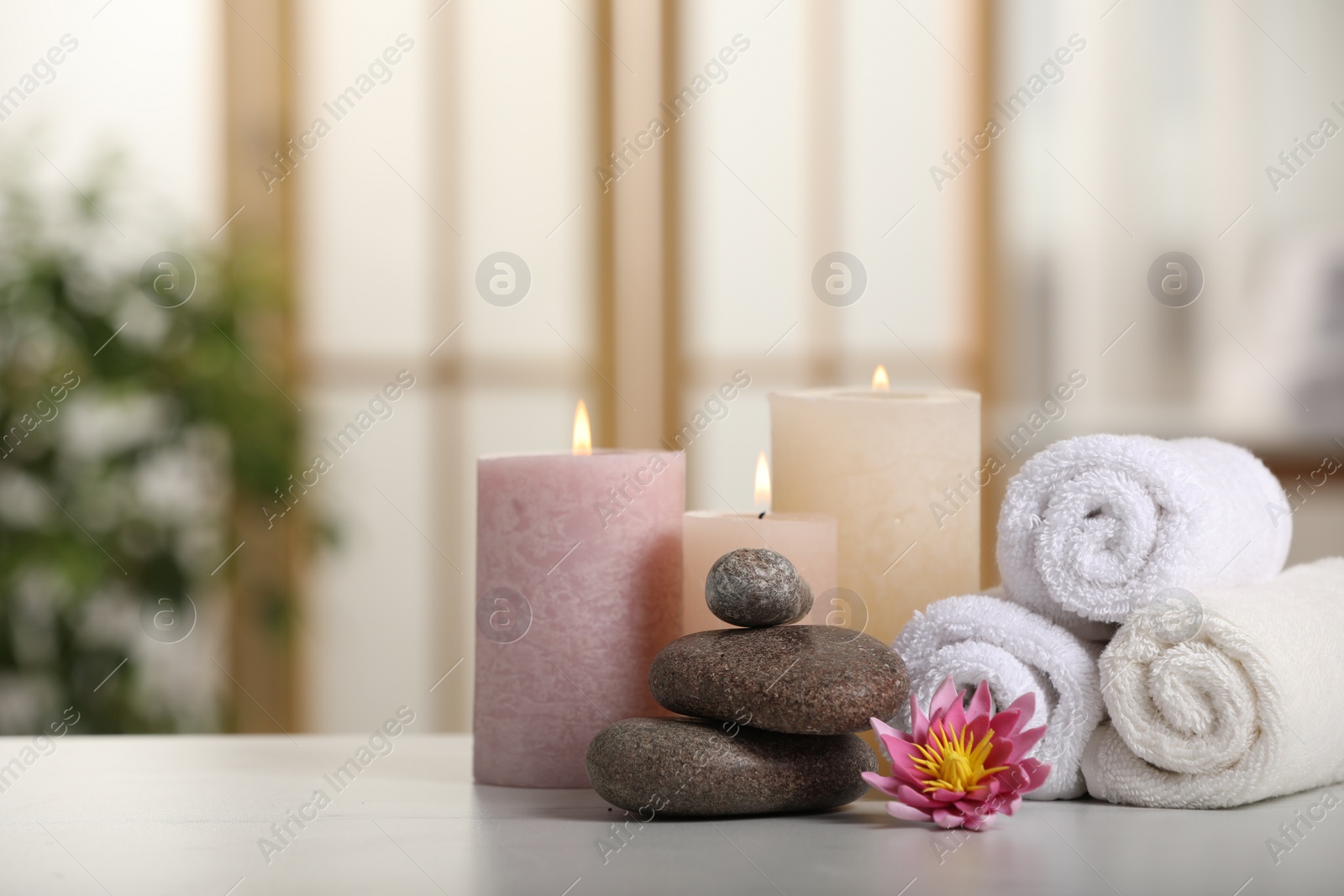 Photo of Spa composition. Burning candles, lotus flower, stones and towels on white table indoors, space for text