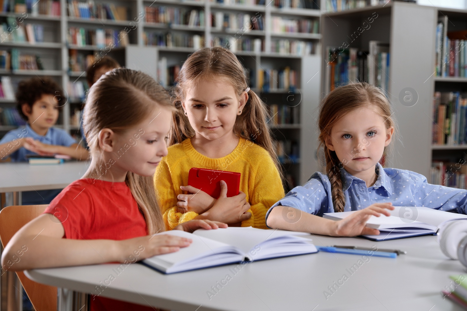 Photo of Happy little girls reading books at table in library