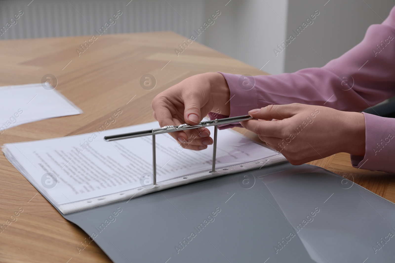 Photo of Woman fixing folder with punched pockets at wooden table, closeup