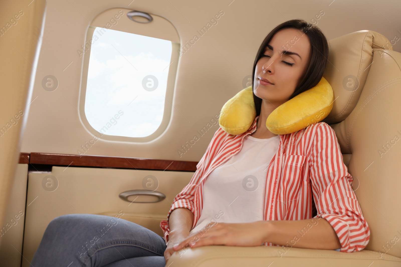 Photo of Young woman with travel pillow sleeping in airplane during flight