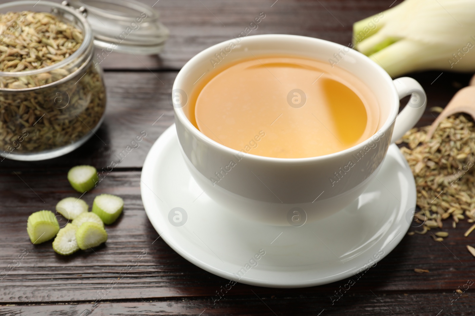 Photo of Fennel tea in cup, seeds and fresh vegetable on wooden table, closeup